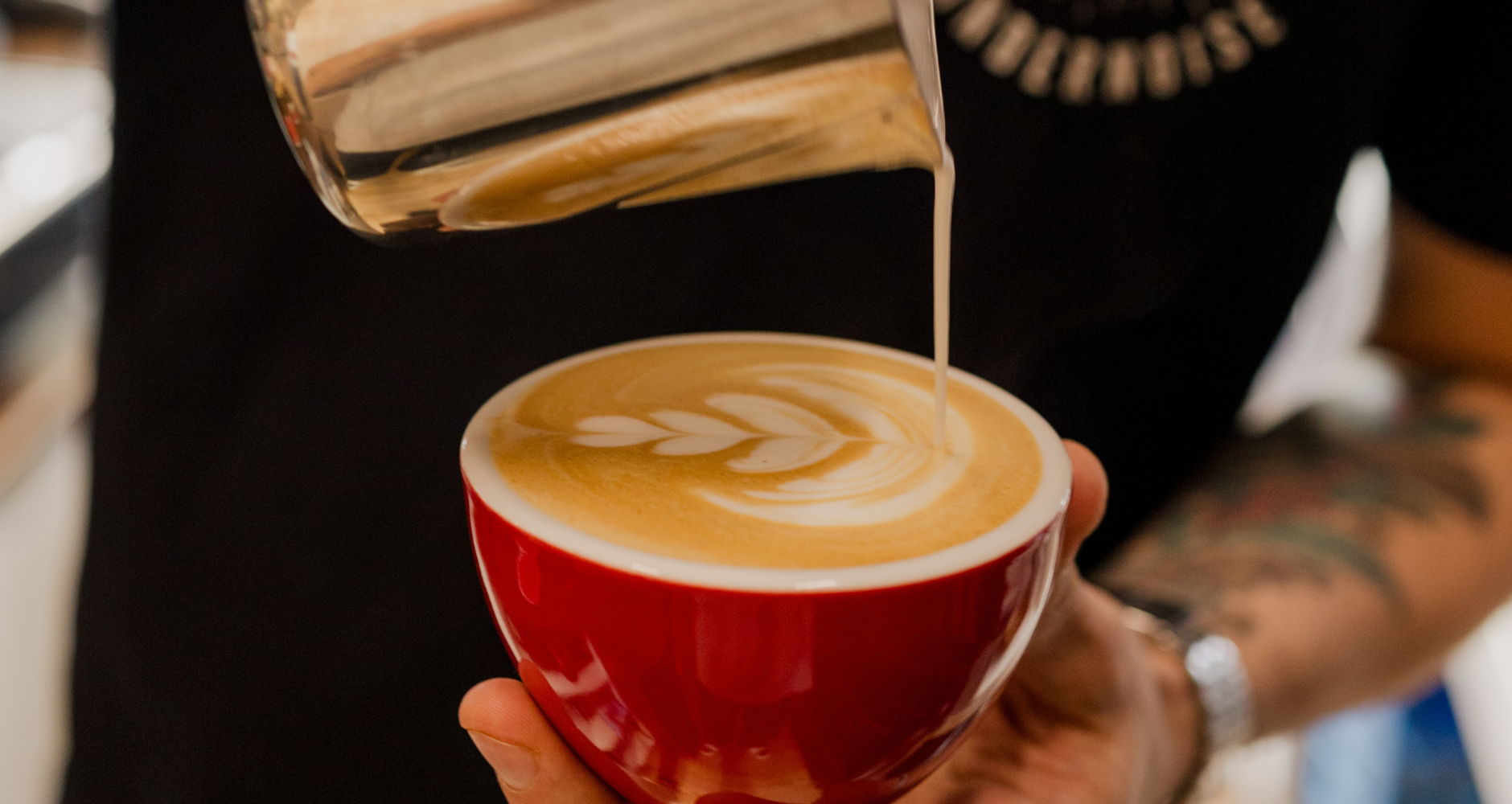 Person pouring a creamy liquid into a red cup with latte art.