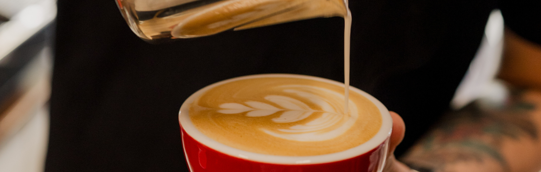 Espresso being poured into a red cup with a visible tattoo on the arm.